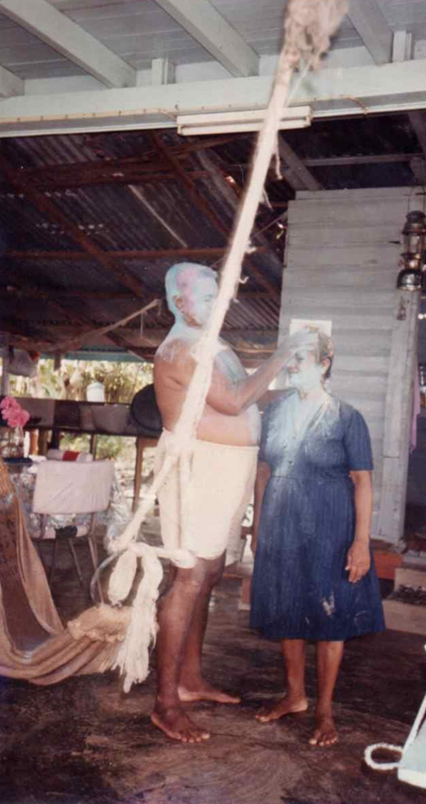 Ugeita's grandfather touches her grandmother's head; they are both covered in powder.