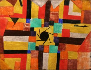 A colorful painting by Paul Klee shows a series of imprecisely interlocking geometric shapes such as rectangles, squares, and triangles, oriented both horizontally and vertically, resembling a pattern on a quilt. A series of angular lines jut from a black circle in the center of the painting, suggesting a rotating motion. A black arrow points toward the right edge of the frame.