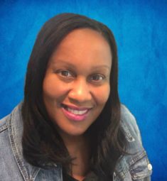 Sonia Adams is an African American woman of Caribbean ancestry. She is brown-skinned, middle-aged with straight, medium-length black hair. In the photo, Sonia is wearing a blue denim jacket. She is smiling in the photo. The background of the photo is colored sky-blue.